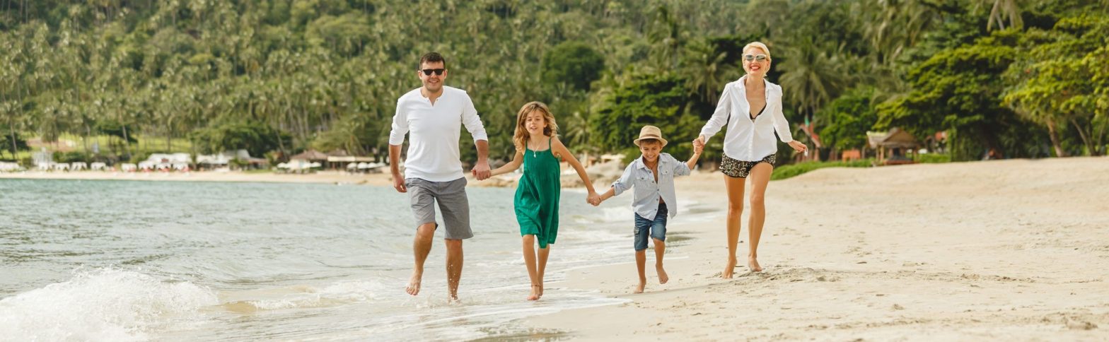 Imagen de frente de una familia con dos hijos dando un paseo por una playa cristalina | Viviendas familiares en Sa Riera